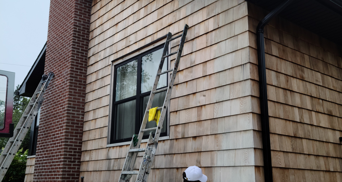 A worker is staining a wooden fence in a residential area on Arlington Avenue in Halifax, Nova Scotia. The worker is wearing protective gear and using a brush to apply the stain.